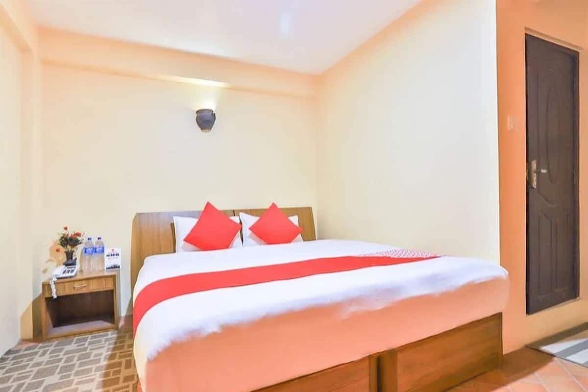 Una habitación de hotel con una cama, una mesita de noche, una lámpara en la pared y una puerta.