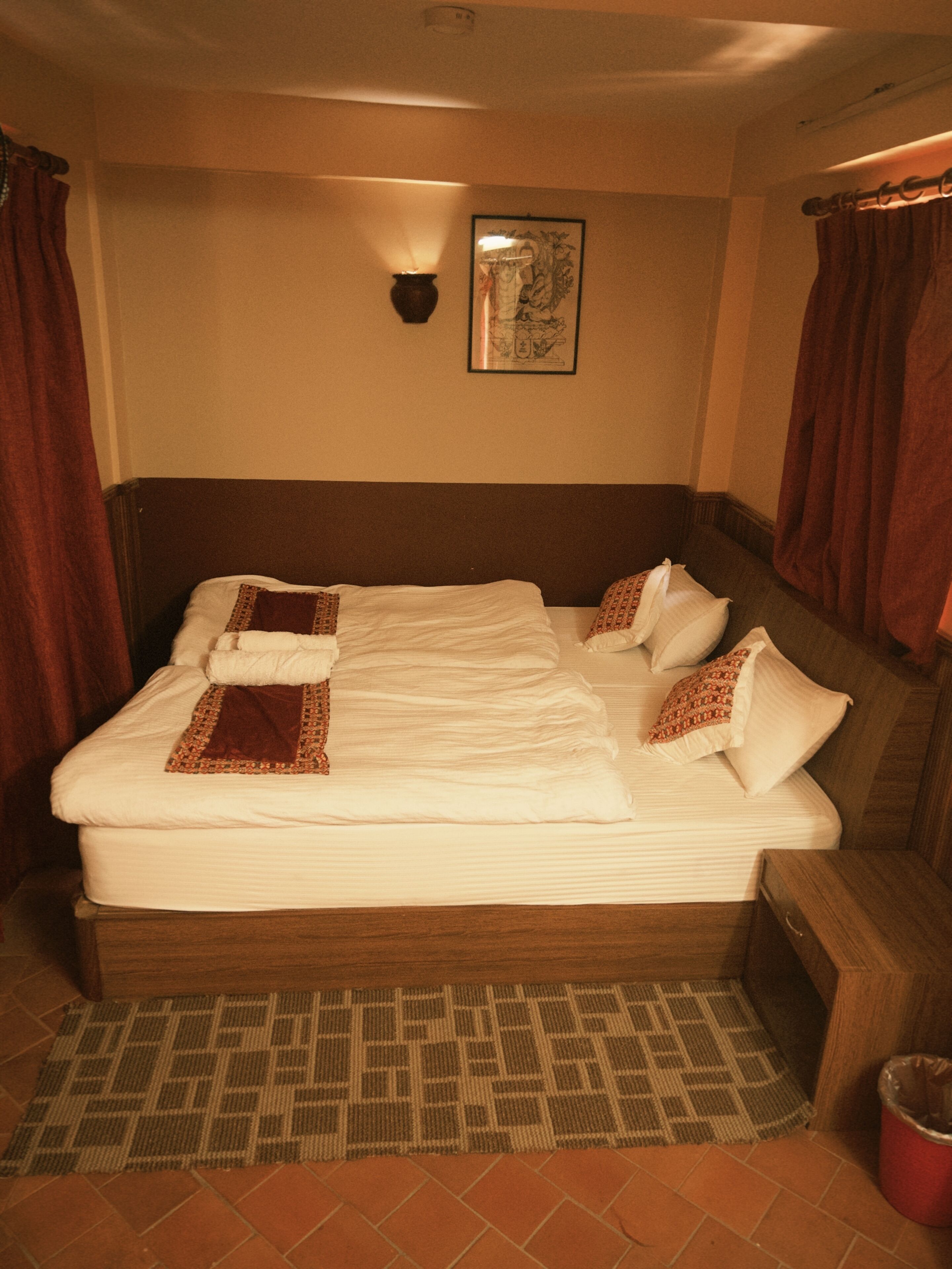 Una habitación de hotel con una cama grande, un cabecero, una lámpara fijada a la pared y una alfombra estampada.