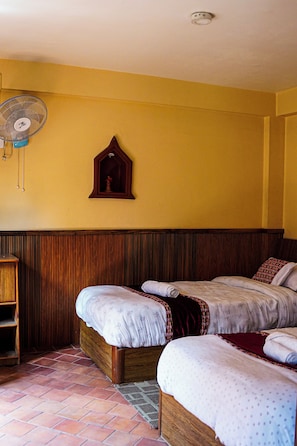 A room with two beds, a wooden headboard, a wall-mounted fan, and a small wooden cabinet. - Hotel Terracotta (Bhaktapur)
