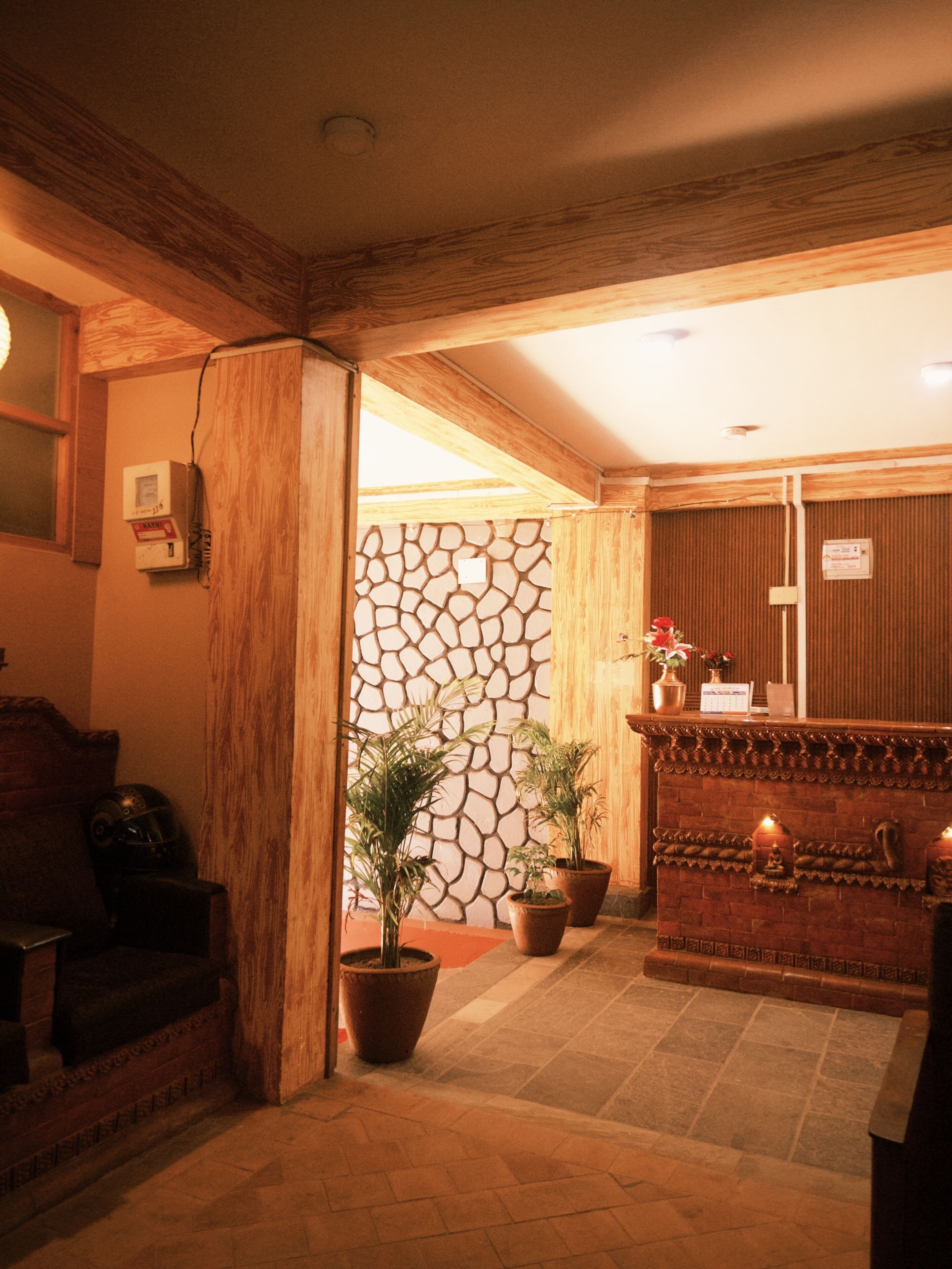 A reception area with a stone wall, wooden reception desk, potted plants, and a seating area with a sofa.