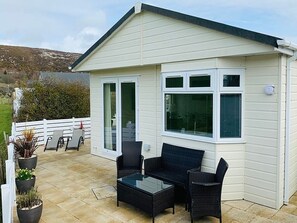 A white building with a patio area featuring wicker furniture and potted plants. - The Warren O7 (Pwllheli)