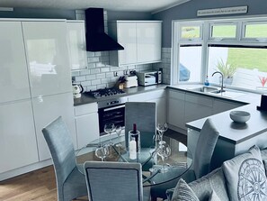 A modern kitchen with white cabinets, a black range hood, a built-in oven, and a window with a view of the outdoors. - The Warren O7 (Pwllheli)