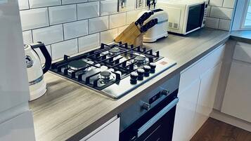 Une cuisine moderne avec des meubles blancs, une cuisinière à gaz, un four à micro-ondes et un grille-pain.