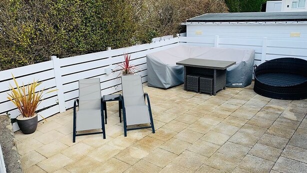 Eine Terrasse mit weißem Zaun, einem überdachten Sitzbereich und einem kleinen Tisch.