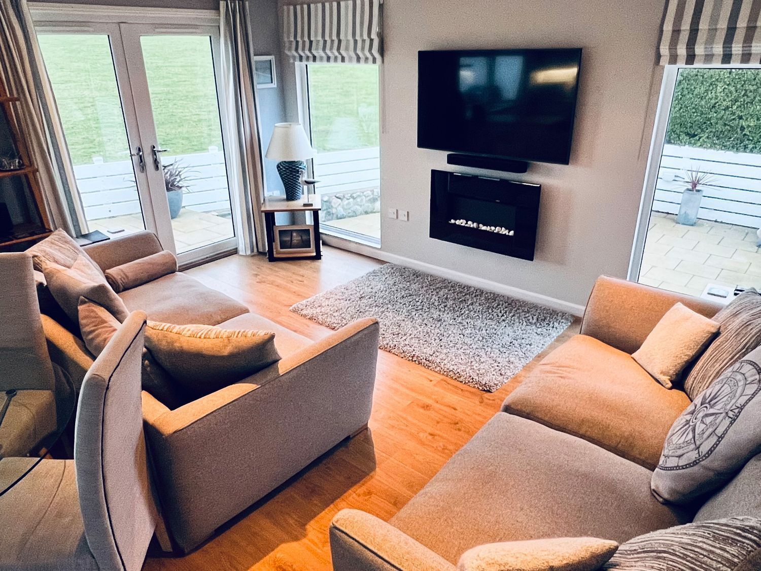 Una sala moderna con un conjunto de sofás, un televisor de pantalla plana montado en la pared y vistas al exterior a través de amplias ventanas.