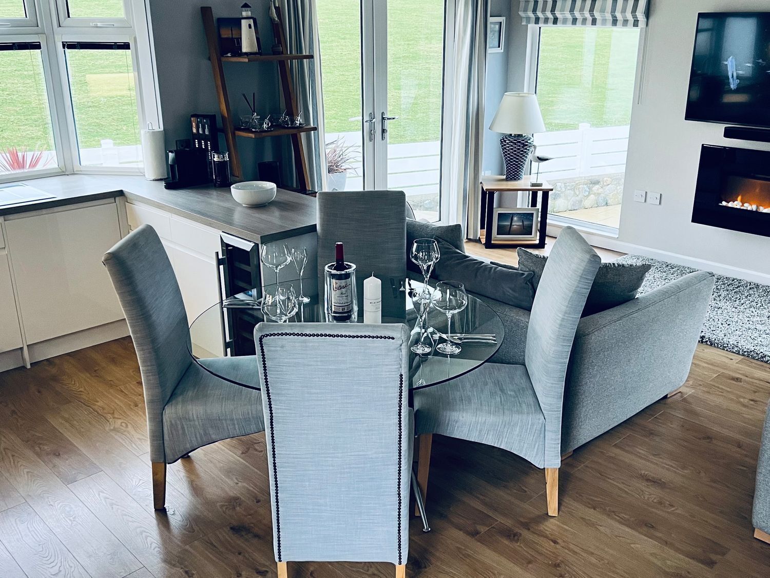 A modern dining area with a glass table, grey upholstered chairs, and a fireplace.