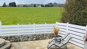 Een terras met een witte hek, een stenen muur en twee loungestoelen.
