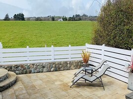 Un patio con cerca blanca, pared de piedra y dos sillones de descanso.