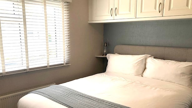 Een slaapkamer met een bed, witte gordijnen, een hoofdbord en een radiator.