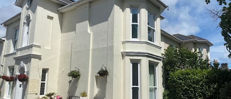 Un bâtiment à deux étages doté de baies vitrées, d’un porche à l’avant orné de plantes en pot et d’une enseigne indiquant un numéro de téléphone.