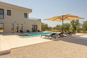 Uma casa moderna com piscina, cadeiras de sol e um guarda-sol grande.