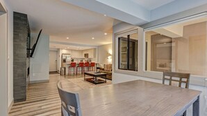 A modern kitchen with white cabinets, a dining area with a wooden table and chairs, and a large window with a view.