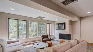 A modern living room with large windows, a fireplace, and a flat-screen TV.