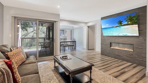 A modern living room with a fireplace, a television, and a dining area with a view of the outdoors.