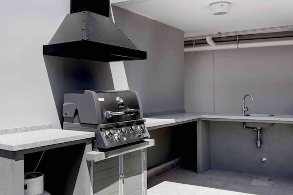 Una cocina exterior moderna con una parrilla integrada, un lavabo y una campana extractora.