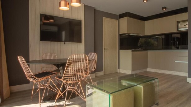 A modern kitchen with a flat-screen TV, a dining area with a glass table and wireframe chairs, and a wooden floor. - Santiago Retreat Plus EXC Modern 2 BR in Las Condes (Santiago)
