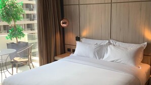 A hotel room with a bed, two bedside tables, a small table with chairs, a potted plant, and a view of a building outside. - Santiago Retreat Plus EXC Modern 2 BR in Las Condes (Santiago)