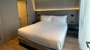 Un lit bien fait dans une pièce au plancher de bois, avec une table de chevet et une porte.