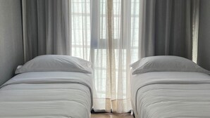 Ein Schlafzimmer mit zwei Betten, einem Fenster mit durchsichtigen Vorhängen und Holzböden.