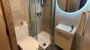 Ein kleines Badezimmer mit Toilette, Dusche, Waschbecken und einem Spiegel mit runder Beleuchtung.