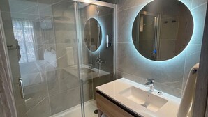 Ein modernes Badezimmer mit einer Duschkabine aus Glas, einem runden Spiegel und einem Holzbadezimmer.