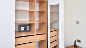 A room with a wooden cabinet with multiple drawers and shelves, a safe, and a small table with a phone and a remote control.