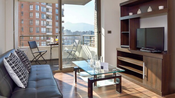 A modern living room with a sofa, a glass coffee table, a TV on a wooden stand, and a balcony with a city view.