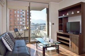 Een moderne woonkamer met een bank, een glazen salontafel, een tv op een houten dressoir en een balkon met uitzicht op de stad.