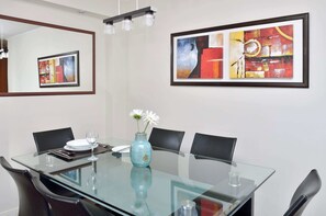 Een vergaderruimte met een glazen tafel, zwarte stoelen, een vaas met bloemen en twee ingelijste abstracte schilderijen aan de muur.