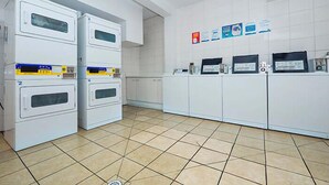 A laundry facility with stacked dryers, a tiled floor, and informational posters on the wall.