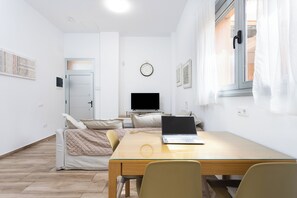 Ein modernes Zimmer mit einem Bett, einem Schreibtisch mit Laptop, einem Fernseher und einem Fenster mit Vorhängen.