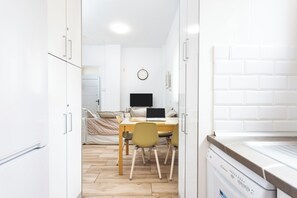 Ein modernes Zimmer mit Bett, Schreibtisch mit Laptop, Waschmaschine und einer Uhr an der Wand.