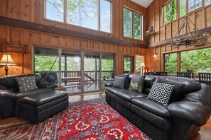 Ein geräumiges Wohnzimmer mit einer großen schwarzen Ledersofa, einem roten Teppich mit Muster und Holzwandverkleidungen.