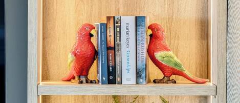 A wooden bookshelf with a green plant, books, and two red bird figurines.