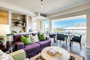 Ein modernes Wohnzimmer mit einem violetten Sofa, einem runden Couchtisch und einem Essbereich mit Stühlen.