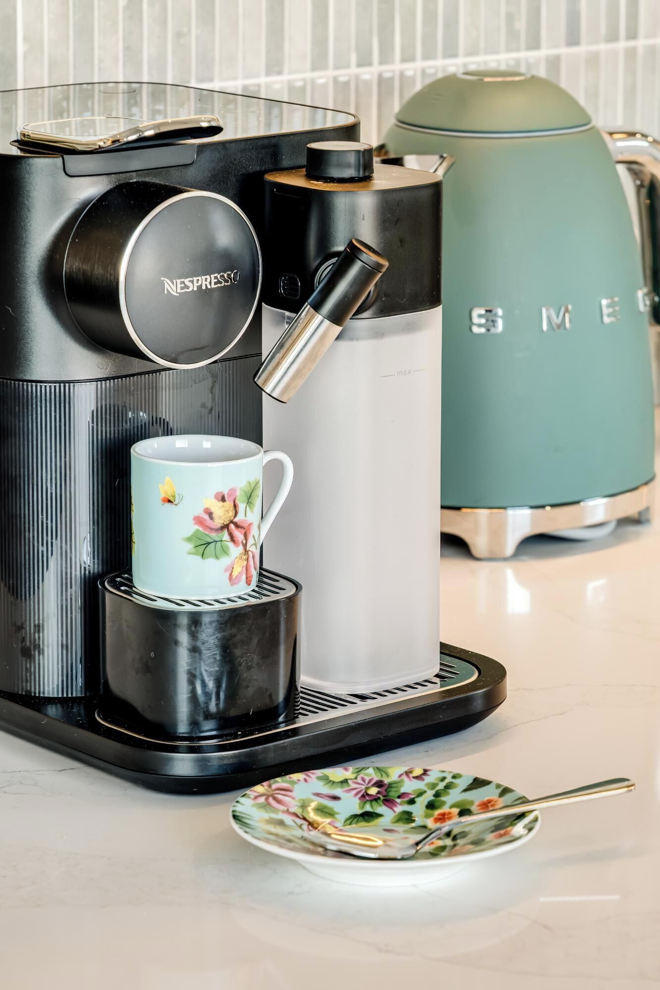 A Nespresso coffee machine with a single cup holder, a water reservoir, and a plate with a spoon.