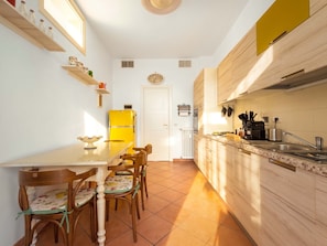 A compact kitchen with a white refrigerator, wooden cabinets, a tiled floor, and a dining area with chairs and a table. - Il Pianoforte Authentic With Balcony (Florence)