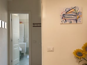 A hallway with a door leading to a bathroom, a light switch, and a wall-mounted artwork of a piano. - Il Pianoforte Authentic With Balcony (Florence)