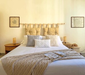 A neatly made bed with a patterned throw, a headboard with multiple pillows, bedside lamps, and framed artwork on the walls. - Il Pianoforte Authentic With Balcony (Florence)