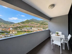 Ein Balkon mit Blick auf eine Stadt und Berge, ein Tisch mit Stühlen und ein Blumentopf.