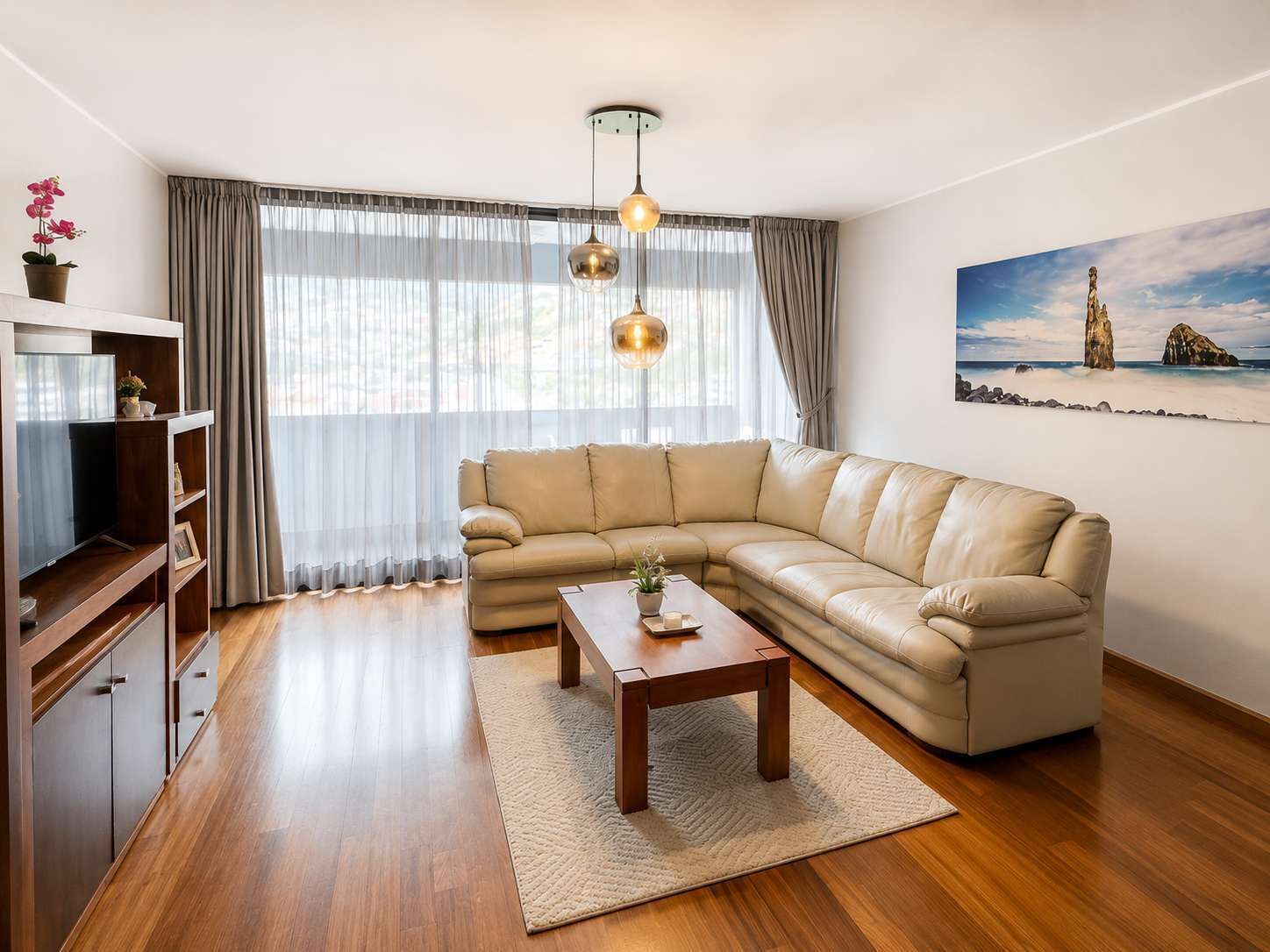 Ein Wohnzimmer mit einer Ledersofa, einem Holztisch und einem Fernseher auf einem Holzboden.