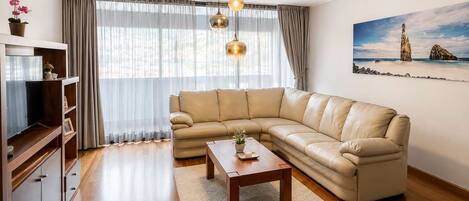 Ein Wohnzimmer mit einer Ledersofa, einem Holztisch und einem Fernseher auf einem Holzboden.