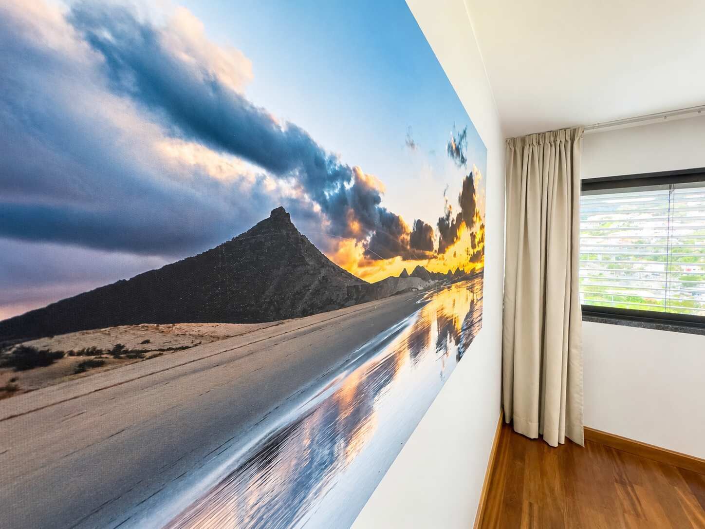 A room with a large wall mural of a mountain landscape, a window with blinds, and a wooden floor.