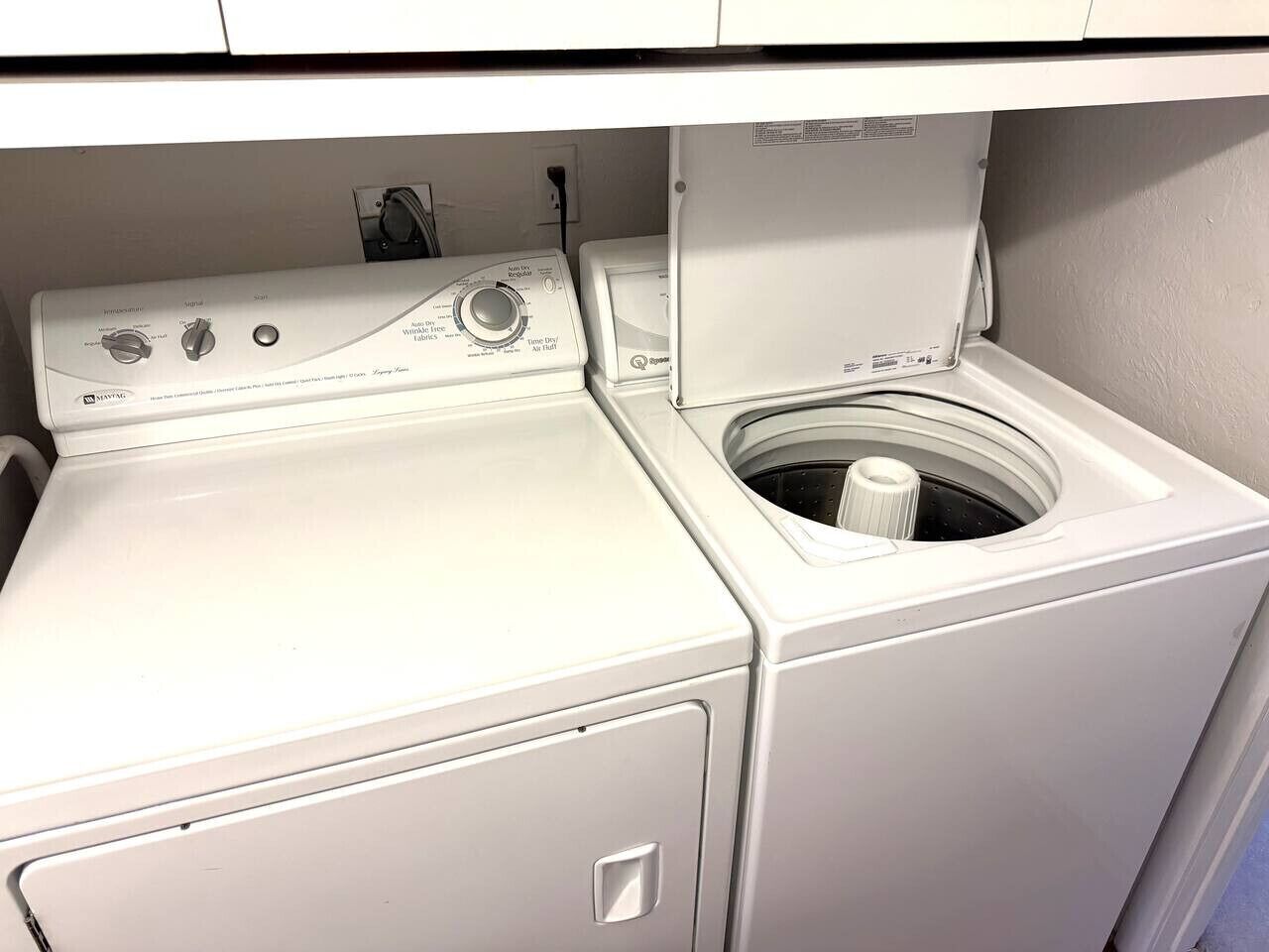 Una lavadora y secadora de carga frontal con panel de control, cable de alimentación e enchufe de pared.