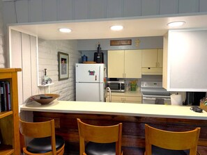 A kitchen with a white refrigerator, microwave, and stove, wooden chairs, and a white countertop. - EagleVail Golf Course Cozy Retreat | Ground Floor (Avon)