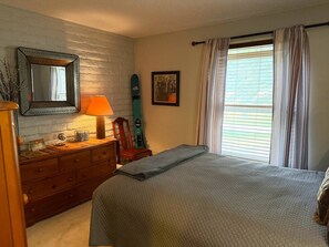 A bedroom with a bed, dresser, lamp, chair, and a window with curtains. - EagleVail Golf Course Cozy Retreat | Ground Floor (Avon)