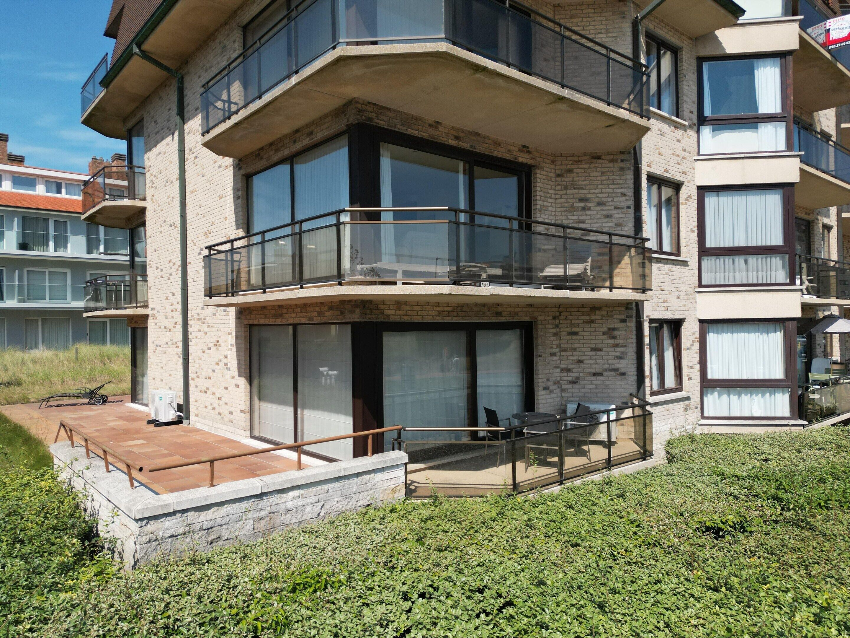 A multi-story residential building with balconies, large windows, and a small outdoor seating area.