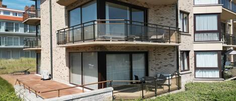 A multi-story residential building with balconies, large windows, and a small outdoor seating area.
