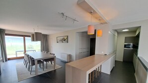 Ett modernt kök med en central köksö, en matplats med bord och stolar samt utsikt genom en glasdörr till ett utomhusområde.