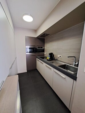 A compact kitchen with built-in appliances, a sink, and a coffee maker. - Family Apartment in Groenendijk (Koksijde)